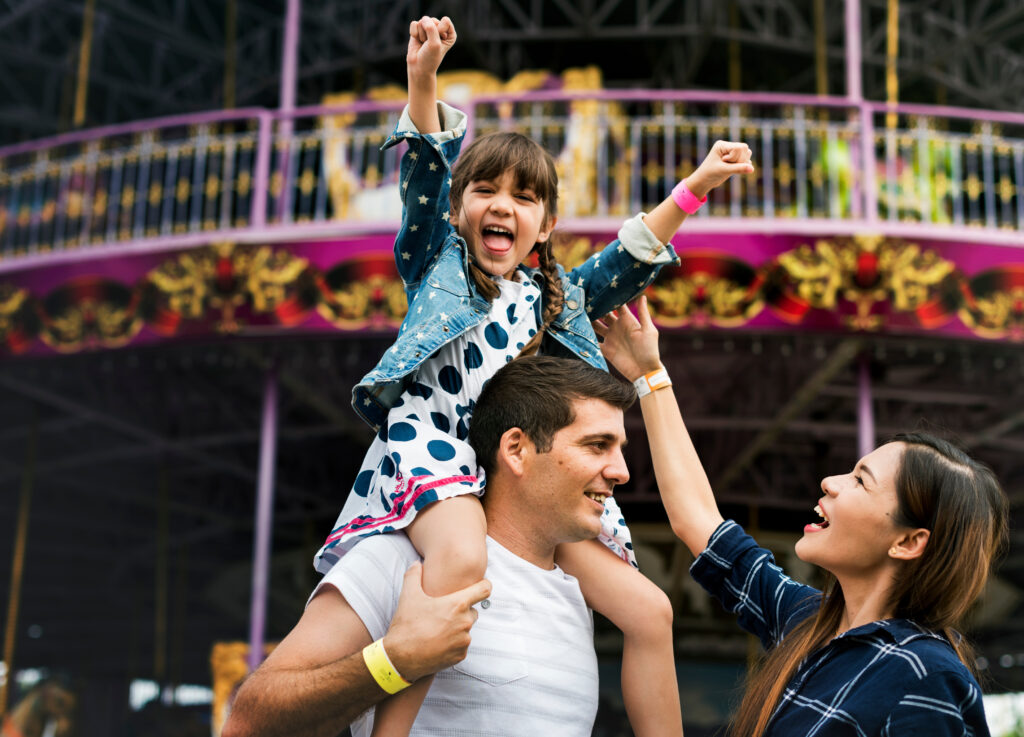 A young girl sits on a man's shoulders with a smile on her face and her hands in the air. A woman smiles while looking up at her. The Role of Experiential Rewards in Cultivating Loyalty